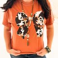 Women’s cow print bow graphic T-shirt by Envy Stylz Wholesale, casual cotton tee with playful animal print design.