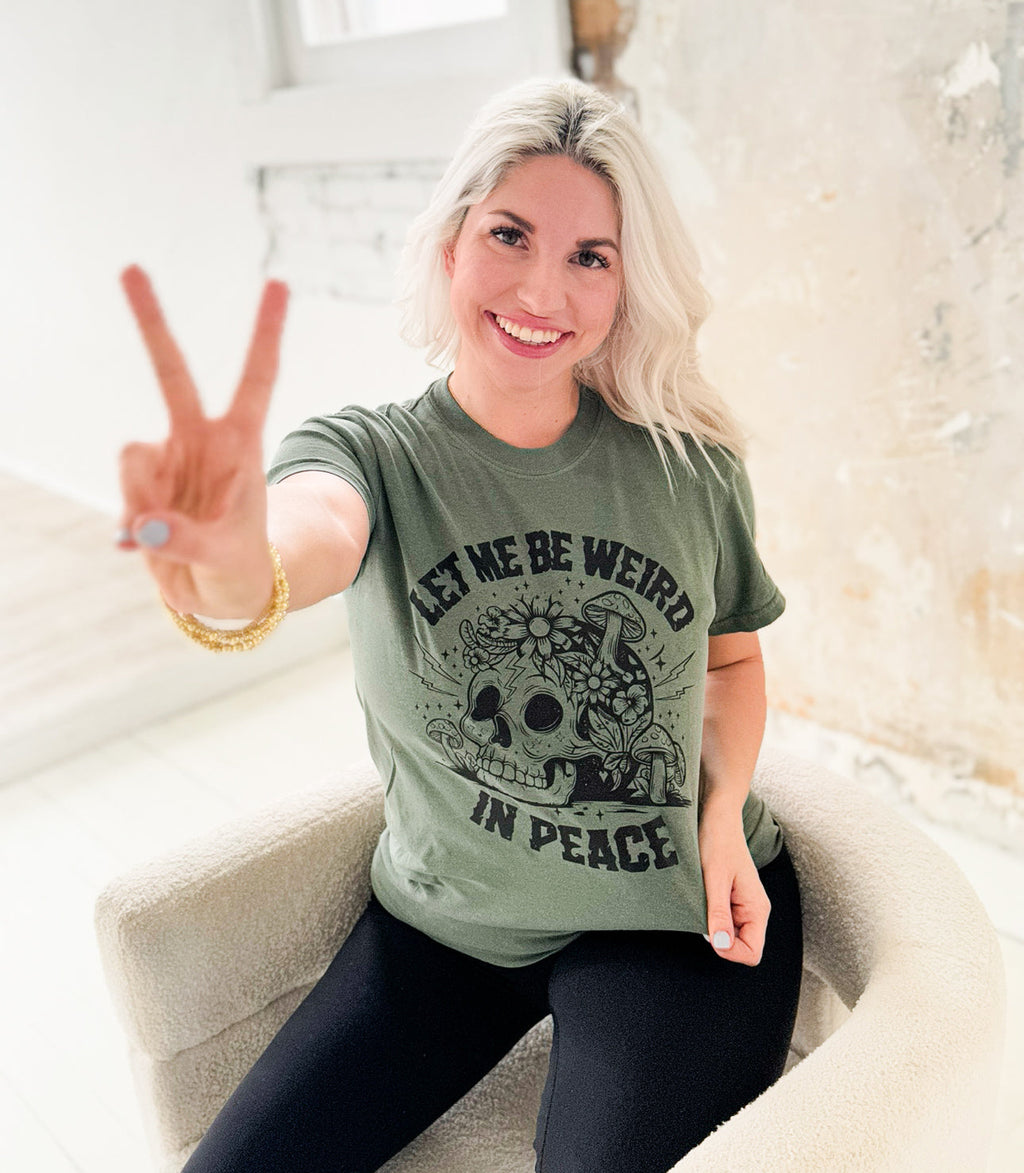 Women’s moss green graphic T-shirt by Envy Stylz Wholesale featuring the “Let Me Be Weird In Peace” design.