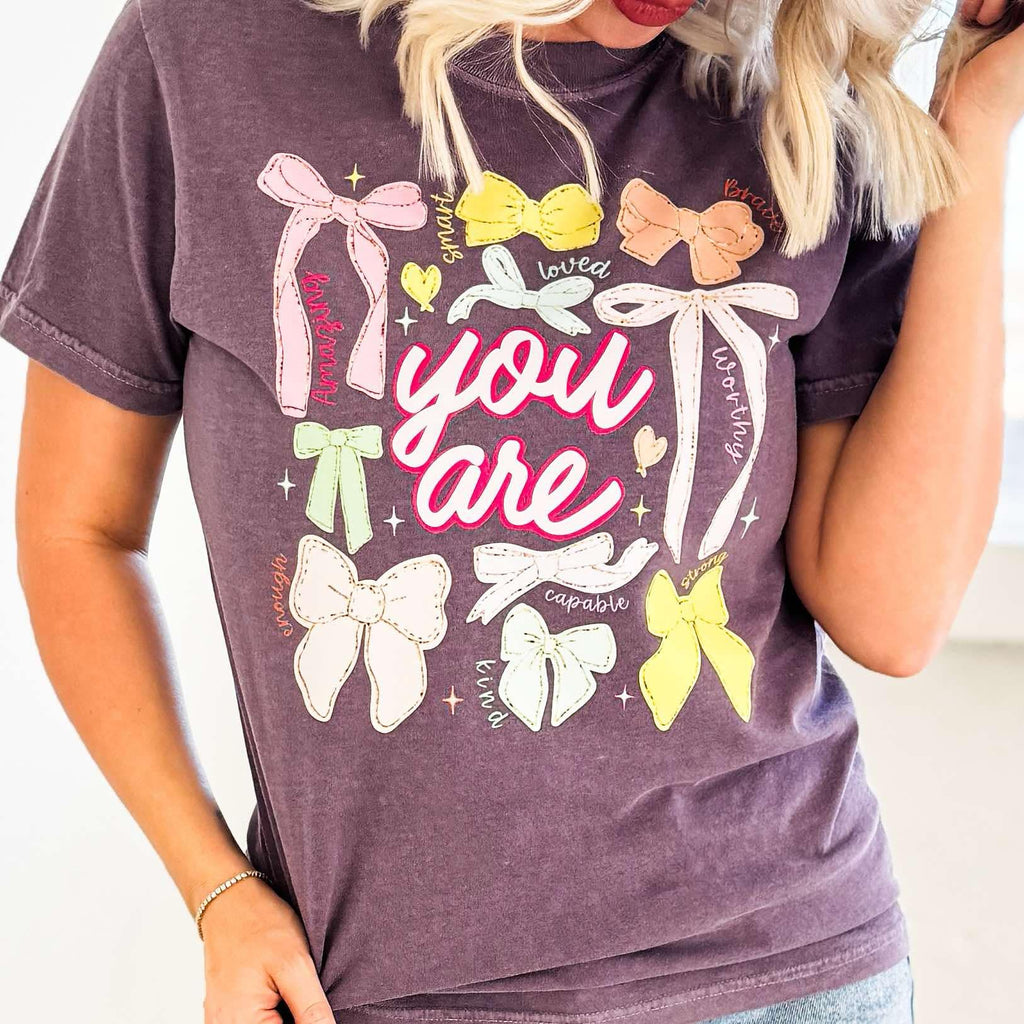 Women’s You Are Colorful Bows graphic T-shirt by Envy Stylz Wholesale, featuring vibrant bow designs on a comfortable tee.