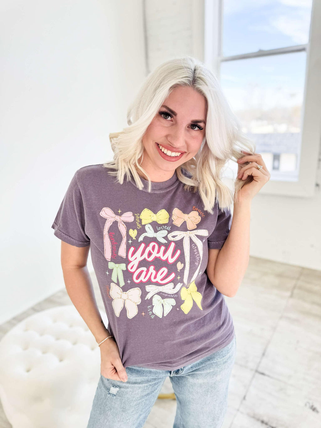 Women’s graphic T-shirt by Envy Stylz Wholesale featuring colorful bow designs on a comfortable grape-colored shirt.