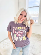 Women’s graphic T-shirt by Envy Stylz Wholesale featuring colorful bow designs on a comfortable grape-colored shirt.