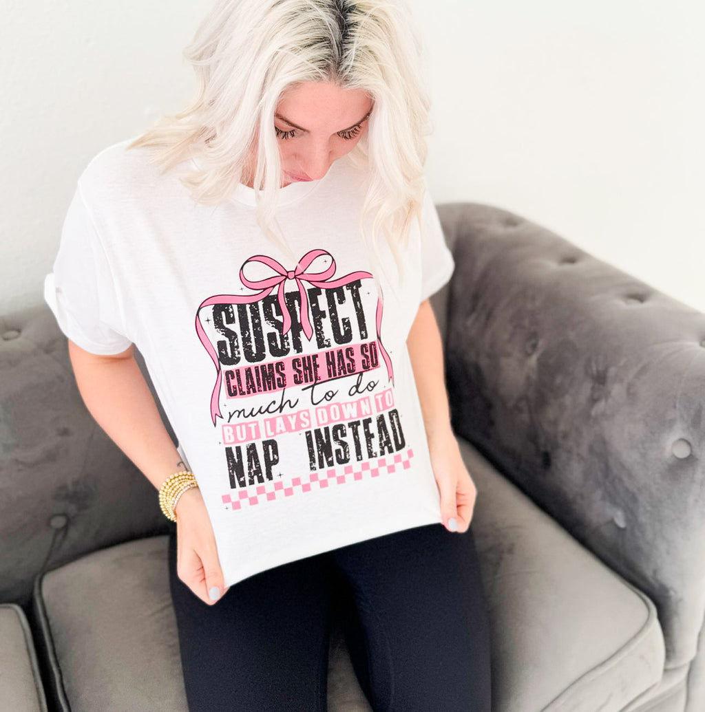 White women's graphic T-shirt by Envy Stylz Wholesale featuring the bold statement "Suspect Claims She Has So Much To Do" in black lettering.