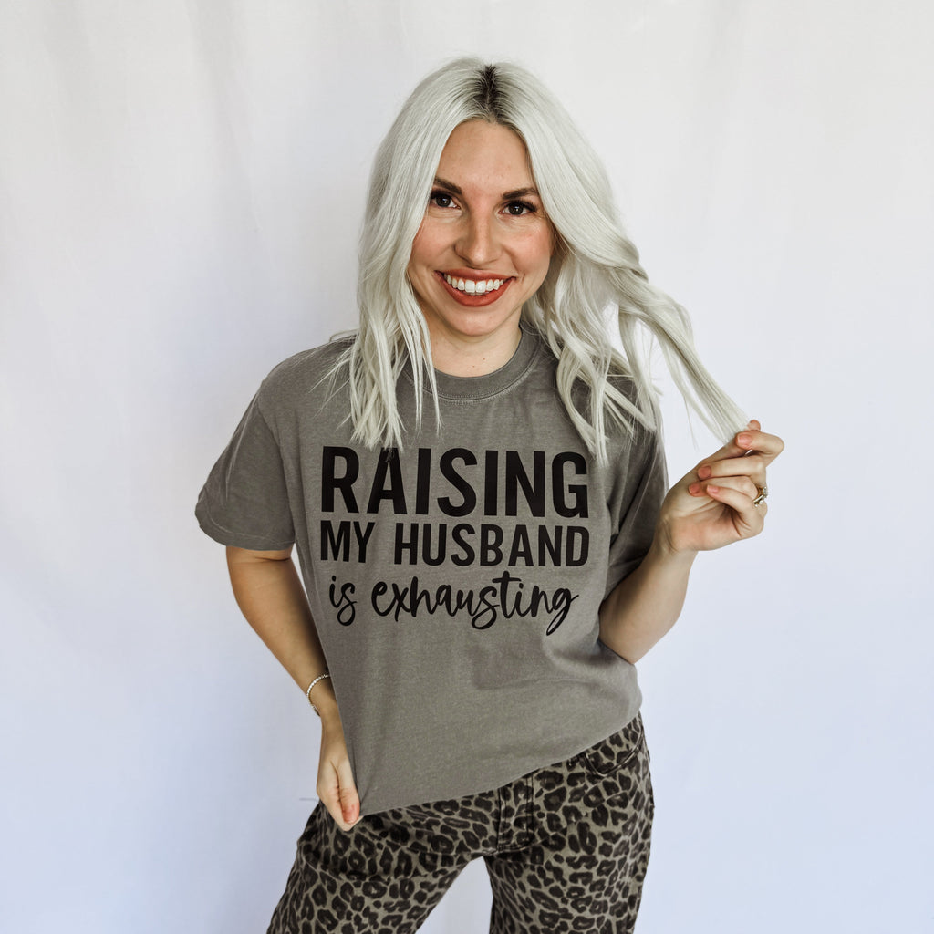 Women’s graphic T-shirt by FestiviTees with “Raising My Husband Is Exhausting” print in comfort colors granite.