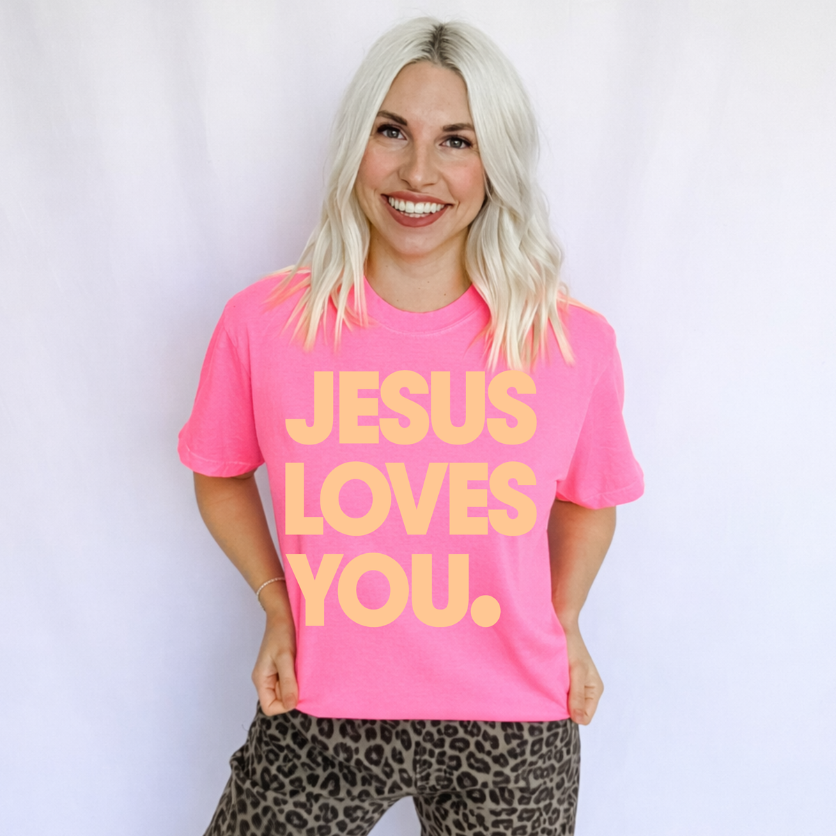 Women’s neon pink T-shirt with "Jesus Loves You" graphic from FestiviTees, casual apparel for a bold statement.