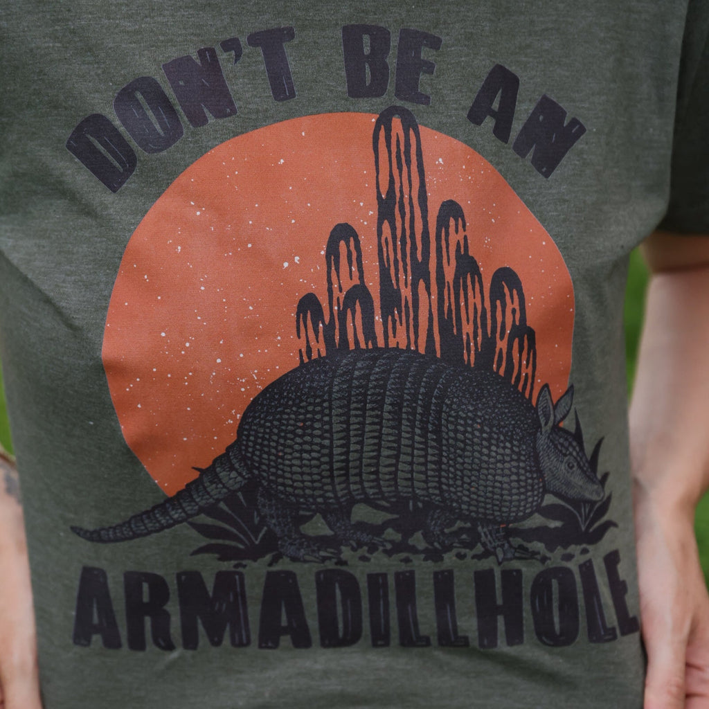 Women’s graphic T-shirt by FestiviTees featuring a playful "Don't Be An Armadillhole" design on a casual shirt.