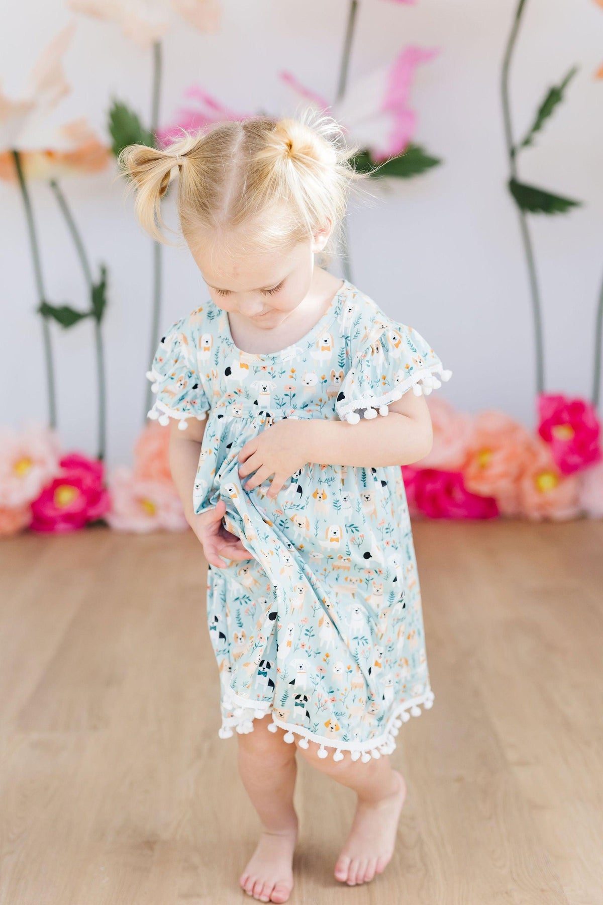 Cute baby girl wearing a pink Mila & Rose Furry Friends Pom Pom Dress with fluffy pom poms for ages 12-24 months.