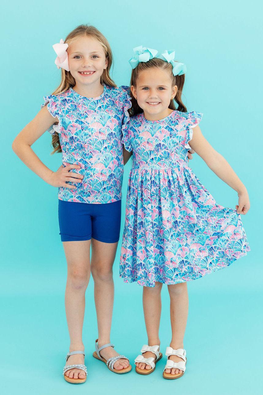 Mila & Rose Seaside Shells short-sleeve ruffle tee for toddlers, light blue with seashell pattern and ruffle detail at the neckline.