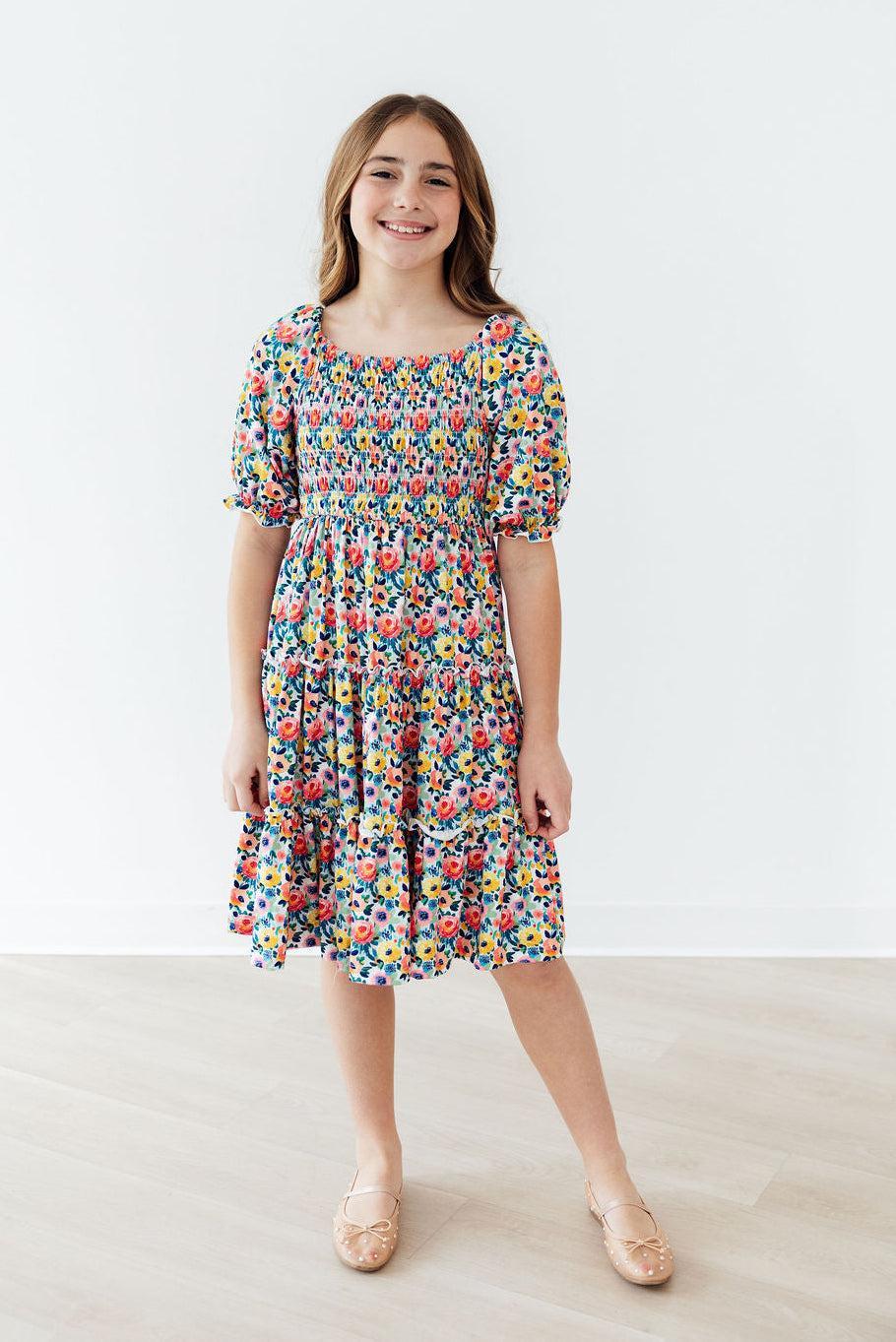 Two-year-old girl wearing a Mila & Rose smocked ruffle dress with floral blossom pattern and ruffled details.