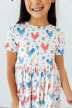 Mila & Rose Rainbow Roosters S/S Pocket Twirl Dress for babies, featuring colorful rooster print and a playful twirl design.