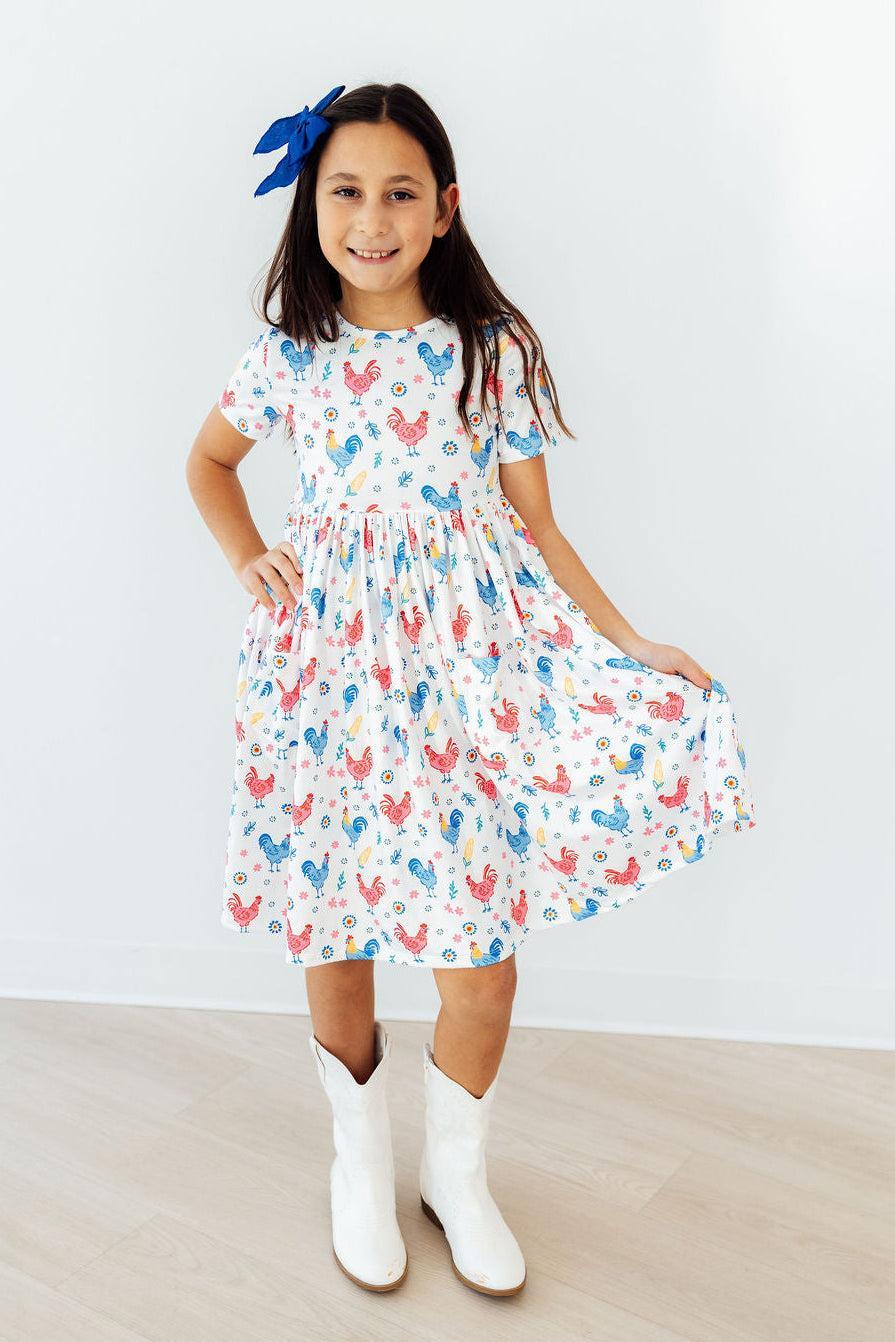 Mila & Rose Rainbow Roosters S/S Twirl Pocket Dress for girls, featuring colorful rooster print and short sleeves.