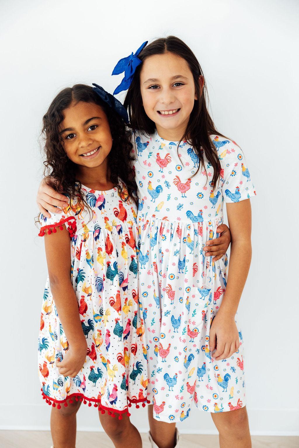 Mila & Rose rainbow rooster print short-sleeve pocket twirl dress for toddlers, featuring colorful rooster pattern and playful design.