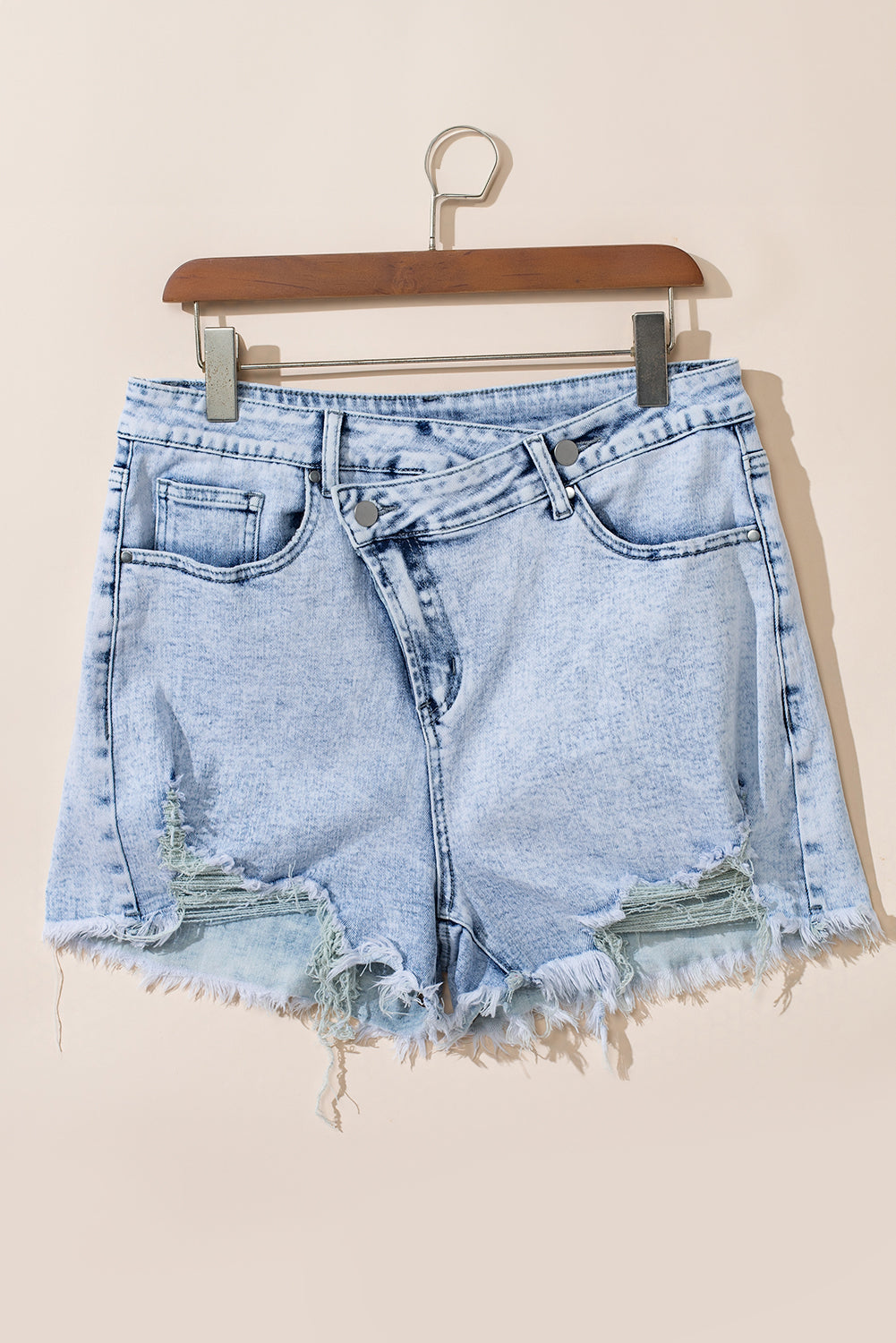 Light blue acid wash denim shorts with crossed raw edges from Mommas Hive, made of cotton, polyester, and elastane.