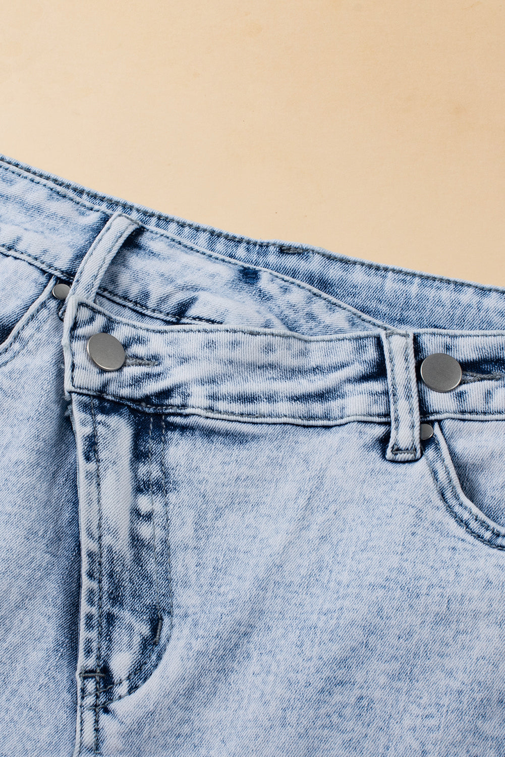 Light blue acid wash denim shorts by Mommas Hive with crossed raw edge design and raw hem, made from cotton, polyester, and elastane.