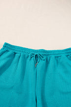Mommas Hive textured ruffle split top and drawstring shorts two-piece set, featuring polyester-elastane fabric and stylish design.
