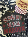 Maroon T-shirt from P&PD Wholesale featuring "On Fridays We Wear Maroon" text, shown on a heather charcoal background.