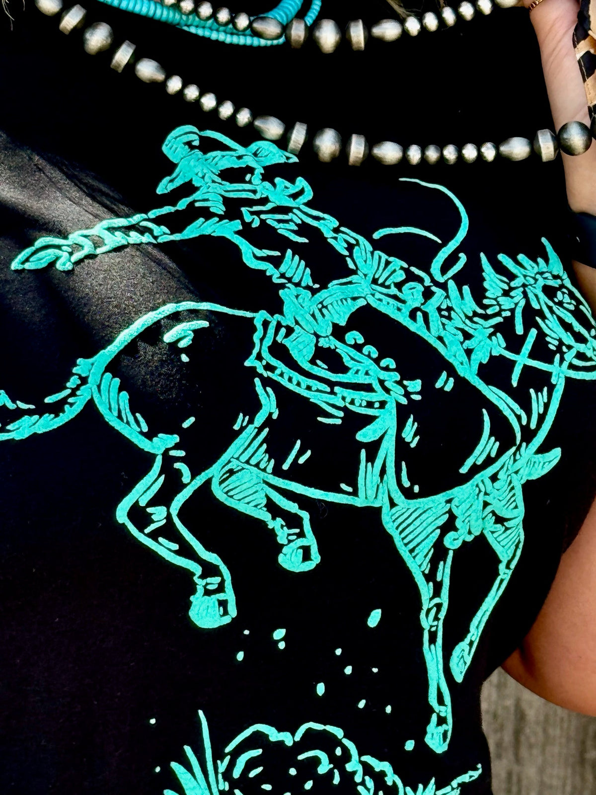Black crewneck tee by Texas True Threads featuring a turquoise puff print design of a Roughrider cowboy.